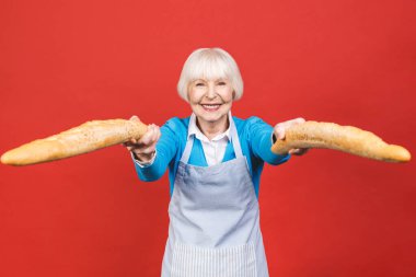 Fransa 'nın tadı. Kırmızı arka planda izole edilmiş taze bir baget ekmeği tutan neşeli yaşlı bir kadının portresi. Fırın kavramı. 