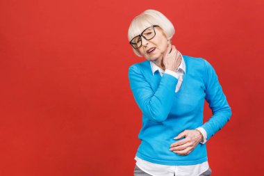 Kırmızı arka planda izole edilmiş boyun ağrısından muzdarip yaşlı bir kadının yakın plan görüntüsü..