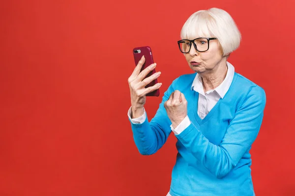 Kızgın yaşlı kadın kırmızı arka planda izole edilmiş telefonla konuşuyor.. 