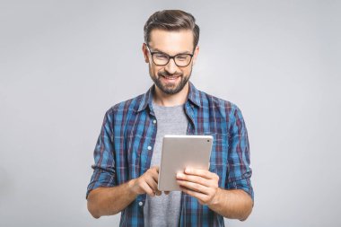Ekose gömlekli mutlu genç adam ayakta ve gri arka plan üzerinde tablet kullanıyor