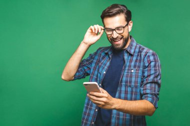 Her zaman görüşüyoruz. Akıllı telefonu tutan ve ona bakan gülümseyen genç bir adam. Yeşil arka planda izole edilmiş cep telefonu kullanan mutlu bir adamın portresi.