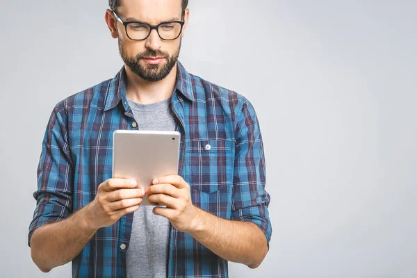 Idea! Thinking young man in plaid shirt standing and using tablet over grey background.