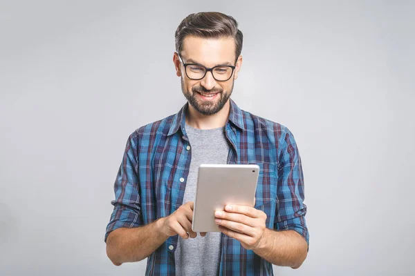 Ekose gömlekli mutlu genç adam ayakta ve gri arka plan üzerinde tablet kullanıyor