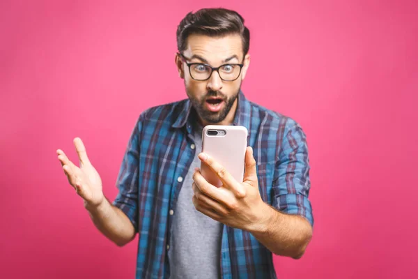 Pembe arka planda izole edilmiş cep telefonuna bakan şaşırmış sıradan bir adamın portresi..