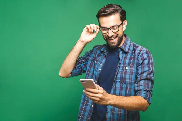 Her zaman görüşüyoruz. Akıllı telefonu tutan ve ona bakan gülümseyen genç bir adam. Yeşil arka planda izole edilmiş cep telefonu kullanan mutlu bir adamın portresi.