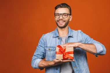 İyi tatiller! Turuncu duvarda izole edilmiş hediye kutusuyla güzel gülüşlü çekici bir adamın sevimli fotoğrafı.. 