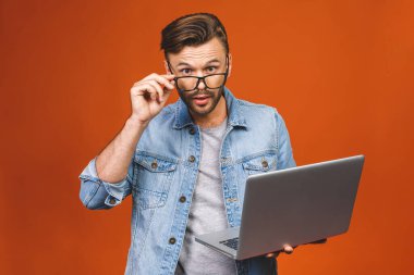 Ayakta duran ve dizüstü bilgisayarı turuncu bir arka planda tutan genç iş adamına şaşırdım..