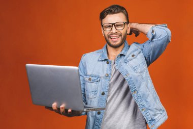 Düşünceli üzgün adam turuncu arka planda izole edilmiş dizüstü bilgisayar kullanıyor.