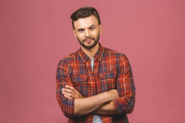 Sıradan bir yakışıklılık. Rahat gömlekli, kendine güvenen, kollarını kavuşturup gülümseyen, pembe arka planda duran yakışıklı bir adam..