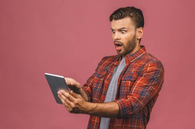 Dijital tablet kullanan mutlu adam sosyal medya haberlerine şaşırmış, şaşırmış müşteri şaşırmış, internetteki galibiyete şaşırmış, pembe stüdyo arka planında izole edilmiş..