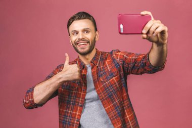 Close up portrait of a cheerful bearded man taking selfie over pink background.