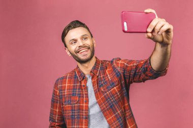 Close up portrait of a cheerful bearded man taking selfie over pink background.