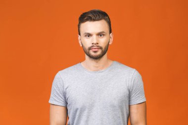 Sıradan bir yakışıklılık. Turuncu arka planda dikilirken rahat gülümseyen kendinden emin genç bir adam..