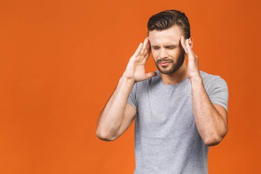 Yakışıklı genç adam turuncu arka planda izole edilmiş, baş ağrısı var..