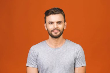 Sıradan bir yakışıklılık. Turuncu arka planda dikilirken gülümseyen kot pantolonlu, kendine güvenen genç bir adam..