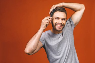 Saçını banyoda tarayan yakışıklı genç adamın portresi. Turuncu arkaplanda izole edilmiş. 