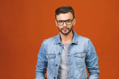 Sıradan bir yakışıklılık. Turuncu arka planda dikilirken gülümseyen kot pantolonlu, kendine güvenen genç bir adam..