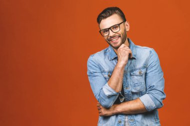 Mutlu genç adam. Sıradan gömlekli yakışıklı bir genç adam portresi. Kollarını kavuşturup gülümsüyor ve turuncu arka planda duruyor..