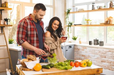 Güzel, genç, gülümseyen mutlu çift evde mutfakta sağlıklı yemekler pişirirken konuşuyor ve gülümsüyor..