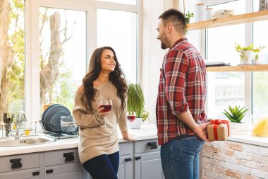 Mutfaktaki çift. Ayakta duran ve arkasında hediye kutusu tutan adam..
