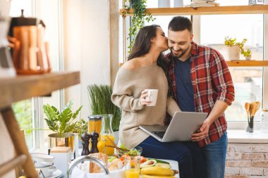 Genç çift laptoplarını kullanarak mutfaktaki yemek tariflerine bakıyorlar.. 
