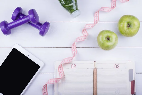 Tablet, defter, detoks, dambıl ve yeşil elma içeren beyaz ahşap masa. Kopya spac ile üst görünüm açısı