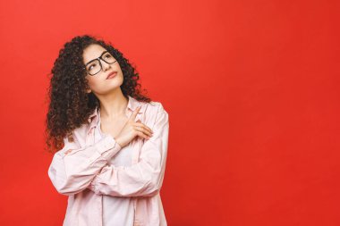 Kırmızı arka planda izole bir şekilde duran genç bayan öğrenci. Kenara bak. İşaret parmağı. 