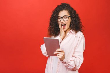 Tabletli genç ve güzel bir kadın heyecanlandı. Kırmızı arka planda izole edilmiş beyaz gömlekli mutlu kız tablet bilgisayar kullanıyor.. 