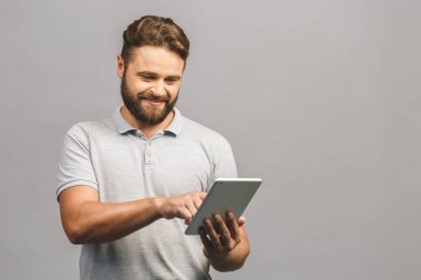 Gri arka planda izole edilmiş tablet kullanan mutlu sakallı genç adam.. 