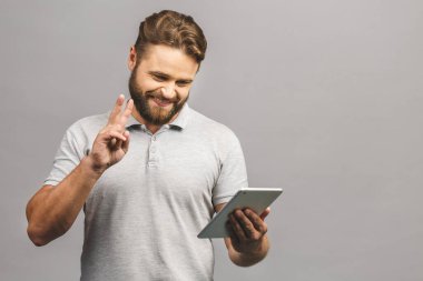 Gri arka planda izole edilmiş tablet kullanan mutlu sakallı genç adam..