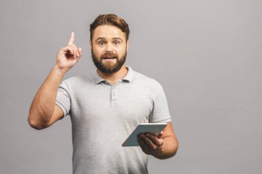 Güzel bir fikrim var! Gri arka planda izole edilmiş tablet kullanan mutlu sakallı genç adam..