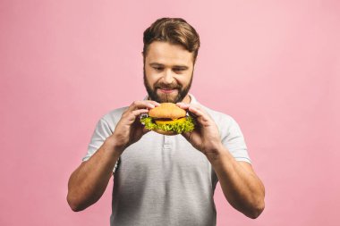Hamburger tutan genç bir adam. Sakallı Gyu fast food yiyor. Burger yararlı bir yemek değildir. Çok aç bir adam. Diyet konsepti. Pembe arka planda izole edilmiş.
