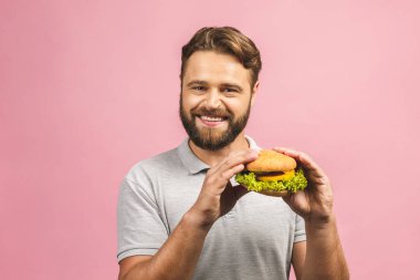 Hamburger tutan genç bir adam. Sakallı Gyu fast food yiyor. Burger yararlı bir yemek değildir. Çok aç bir adam. Diyet konsepti. Pembe arka planda izole edilmiş. 
