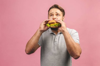 Hamburger tutan genç bir adam. Sakallı Gyu fast food yiyor. Burger yararlı bir yemek değildir. Çok aç bir adam. Diyet konsepti. Pembe arka planda izole edilmiş.
