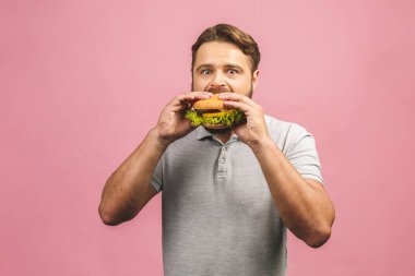 Hamburger tutan genç bir adam. Sakallı Gyu fast food yiyor. Burger yararlı bir yemek değildir. Çok aç bir adam. Diyet konsepti. Pembe arka planda izole edilmiş.