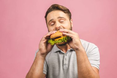 Hamburger tutan genç bir adam. Sakallı Gyu fast food yiyor. Burger yararlı bir yemek değildir. Çok aç bir adam. Diyet konsepti. Pembe arka planda izole edilmiş.