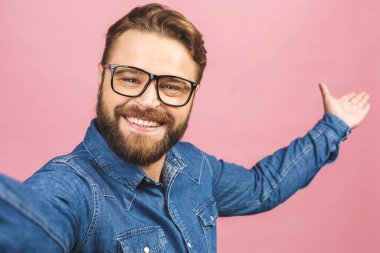 Selfie 'ye bayılırım! Tişörtlü yakışıklı bir genç, elinde kamera ve selfie çekiyor ve pembe arka planda dikilirken gülümsüyor.. 