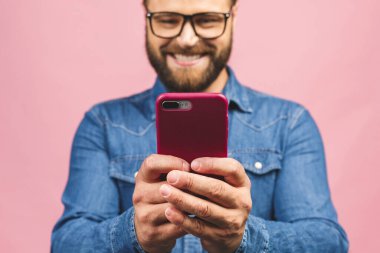 Gözlüklü mutlu genç adam pembe arka planda SMS yazıyor..