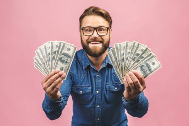 Büyük ikramiyeyle kazanan mutlu. Keyifli sakallı iş adamı pembe arka planda izole edilmiş kameraya bakarken sıradan bir şekilde elinde para tutuyor..