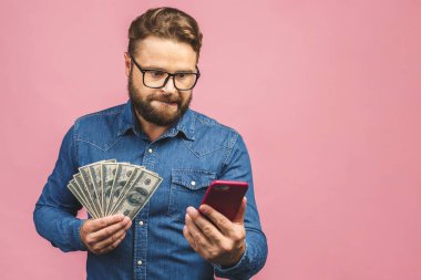 Mutlu galip! Sakallı mutlu adam para ödülünü gösteriyor ve pembe arka planda izole edilmiş akıllı telefonu kullanıyor..