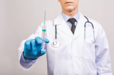 Mavi eldivenli kıdemli doktor gri arka planda izole edilmiş enjeksiyon için tıbbi bir şırınga tutuyor.. 