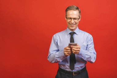 Kırmızı arka planda izole edilmiş akıllı telefondan resmi yazı yazan kıdemli iş adamı. Cep telefonu kullanan mutlu bir iş adamının portresi. Tatmin olmuş lider e- postaları kopyalama alanı ile kontrol ediyor.