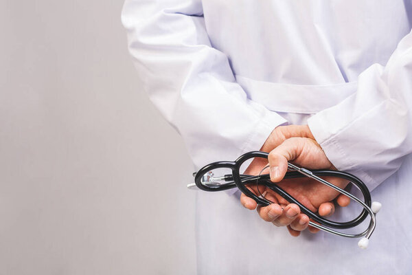 Male medicine therapeutist doctor hands crossed holding stethoscope closeup isolated on grey background. Medical help or insurance concept. 