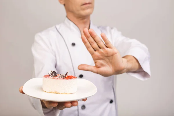 Senior male chef cook or baker man in white uniform posing isolated on white background. Cooking food concept. Showing stop gesture to plate with cake