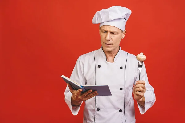 Kıdemli Bir Aşçının Portresi Elinde Yemek Tarifi Kitabı Kırmızı Arka — Stok fotoğraf