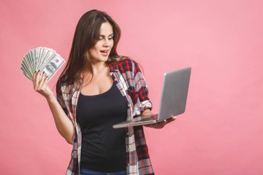 Elinde para banknotları tutan neşeli genç bir kadının portresi ve pembe arka planda izole edilmiş kutlamayı. Laptop kullanılıyor.