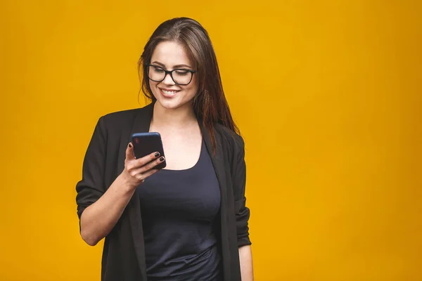 Gözlüklü gülümseyen iş kadınının portresi. Elinde akıllı telefon var ve sarı arka plana bakıyor. Telefon kullanılıyor. 