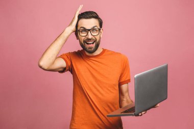 Kendine güvenen bir iş uzmanı. Dizüstü bilgisayarı olan ve pembe arka planda dururken gülümseyen kendine güvenen genç, şaşkın, yakışıklı bir adam..