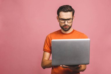 Kendine güvenen bir iş uzmanı. Pembe arka planda dikilirken elinde dizüstü bilgisayarla kendine güvenen, düşünceli, yakışıklı bir genç adam..