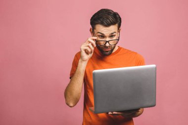 Kendine güvenen bir iş uzmanı. Dizüstü bilgisayarı olan ve pembe arka planda dururken gülümseyen kendine güvenen genç, şaşkın, yakışıklı bir adam..